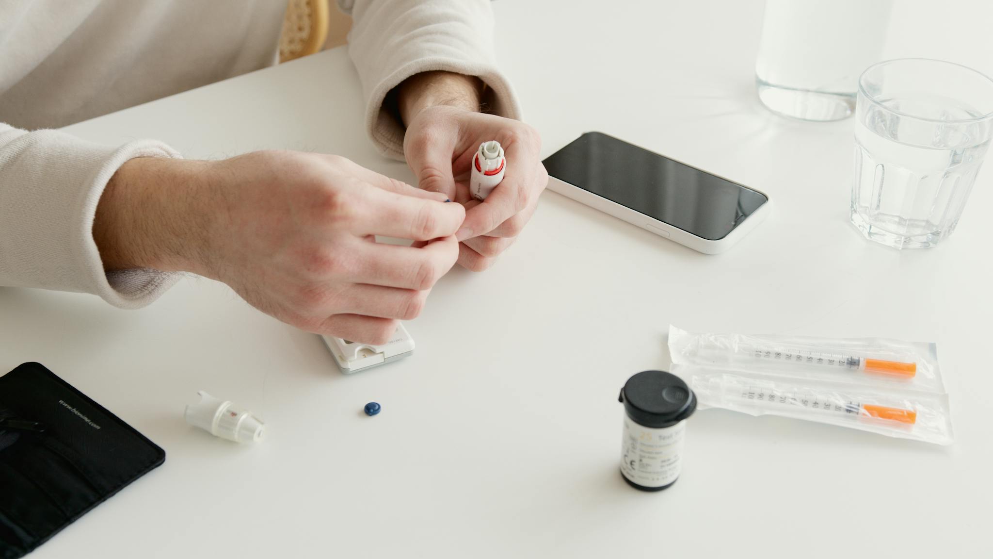 Person preparing insulin injection with medical devices and glucometer on a table.